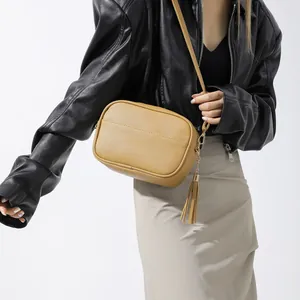 Khaki pebbled PU leather crossbody camera bag with gold tassel charm on female model