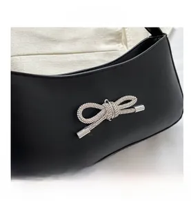 Close-up of elegant black underarm bag with a rhinestone-studded bow and matte leather