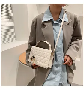 Détail d'un sac bandoulière beige matelassé avec fermoir doré élégant et pompon en chaîne