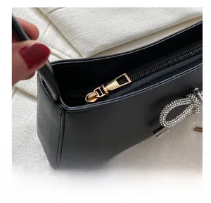 Close-up of black leather underarm bag featuring smooth gold zipper and rhinestone bow detail