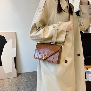 Retro brown leather crossbody bag with gold triangular lock shown on khaki trench coat