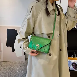 Fashionable emerald green crossbody bag with golden lock on a khaki trench coat