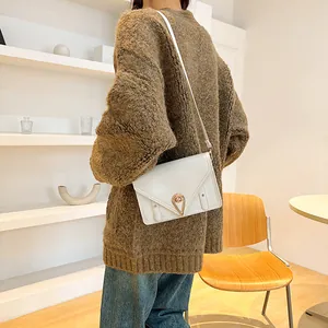Minimalist creamy white leather crossbody bag worn by a model in a modern interior setting