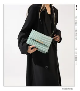 Detail of mint green quilted crossbody bag with gold hardware worn by a model in black suit