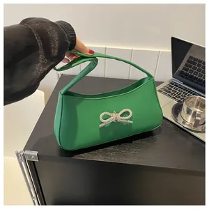 Detail of green shoulder bag with silver rhinestone bow on a minimalist background
