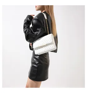 Close-up of a white quilted crossbody bag with a gold chain strap on a black leather outfit