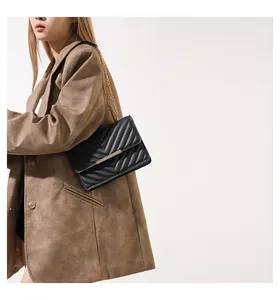 Detail of a black quilted leather crossbody bag with gold chain and metal lock on a model