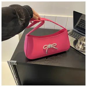 Detail of a bright pink shoulder bag with a rhinestone bow and smooth leather texture