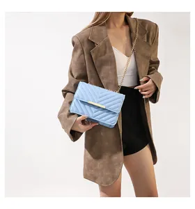 Light blue chevron quilted crossbody bag with gold chain strap worn by a model in a suit