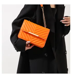 Detail of orange quilted crossbody bag with gold chain strap on a black blazer