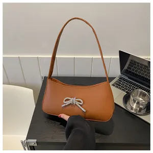 Close-up of brown leather underarm bag featuring a sparkling silver rhinestone bow detail