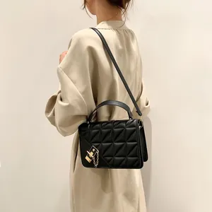 Sac bandoulière matelassé noir élégant avec chaîne dorée porté sur un manteau beige