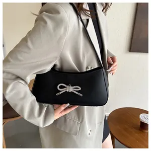 Detailed view of black matte leather underarm bag with silver rhinestone bow on model