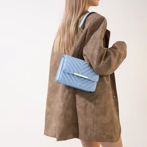 Light blue quilted shoulder bag with gold clasp shown on a model wearing a brown blazer
