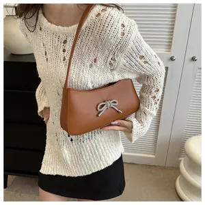 Brown leather shoulder bag with silver bow accent worn by model in casual setting