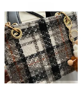 Detail shot of houndstooth tweed texture and plush pom-pom charm on a small tote bag