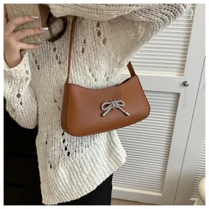 Detail of a brown leather baguette bag with a sparkling rhinestone bow on a model
