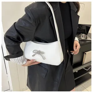 Close-up of white leather hobo bag with sparkling diamond bow buckle in a chic setting