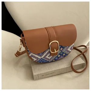 Close-up of saddle bag featuring brown leather, blue plaid fabric, and golden horseshoe buckle