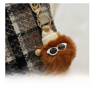 Macro shot of brown faux fur pom-pom charm with knitted hat and gold lobster clasp