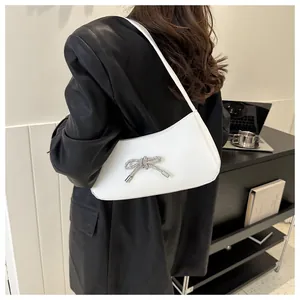 Close-up of a white underarm bag with a crystal bow worn by a model in black leather jacket