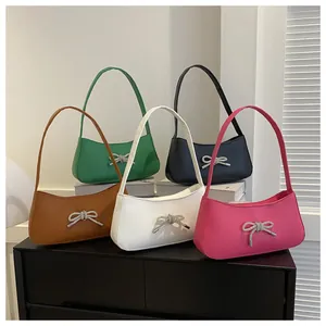 Group shot of colorful leather baguette bags with rhinestone bow accents on a display stand