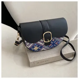 Close-up of ethnic patterned crossbody saddle bag with golden buckle on a book