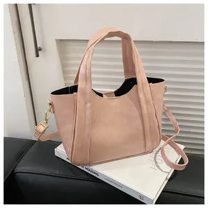 Detail of light pink suede tote bag with gold hardware on artistic white book props