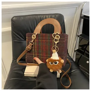 Detail view of plaid wool handbag with brown leather straps and cute plush monster charm