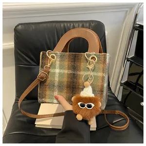 Detail of wool houndstooth crossbody bag with green check pattern and plush monster charm