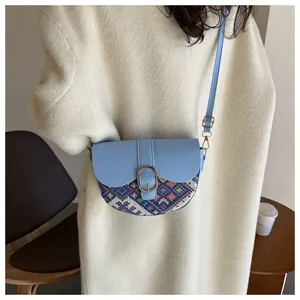 Detail of light blue saddle bag with ethnic embroidery worn over a white wool coat