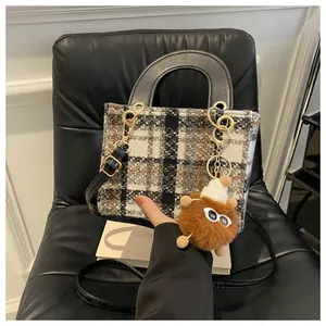Detail of tweed houndstooth handbag with black handle and brown plush doll charm