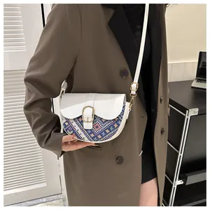 Detailed close-up of ethnic weave stitching and gold buckle on white saddle bag