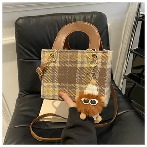 Detail of wool houndstooth handbag with brown leather strap and plush pompom charm