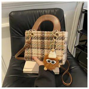 Brown houndstooth crossbody bag with plush monster charm on a white book display