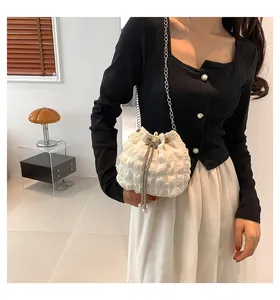 Details einer weißen Plissee-Beuteltasche mit silberner Metallkette an einem Model