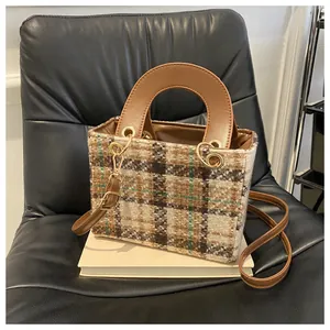 Detailed view of the houndstooth tweed texture and brown leather handle on a crossbody bag