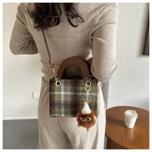 Detail of tweed houndstooth crossbody bag with green check pattern and plush monster charm