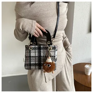 Detail view of houndstooth plaid pattern purse with plush charm and leather handle