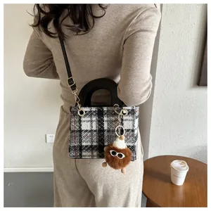 Detail of wool houndstooth crossbody bag with black leather handle and plush charm accessory