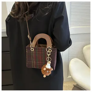 Detail of red and green plaid wool crossbody bag with a plush bear charm on its side