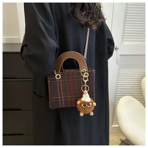 Detail of red and green plaid wool crossbody bag with plush monster charm and leather handle