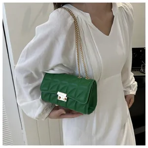 Détail du sac bandoulière vert émeraude avec fermoir doré sur une robe blanche