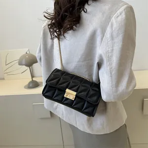 Sac bandoulière matelassé noir avec chaîne dorée porté sur un blazer gris