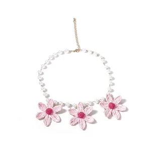 Dettaglio di margherite in rafia rosa su collana di perle bianche con chiusura dorata