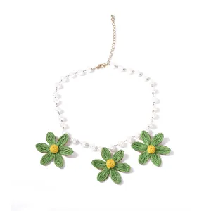 Primo piano della collana di perle con tre fiori in rafia verde fatti a mano