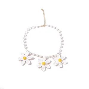 Dettaglio di margherite in rafia intrecciata su collana di perle con chiusura in oro