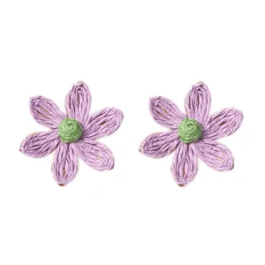 Dettaglio degli orecchini a margherita in rafia viola intrecciata con centro verde