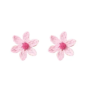 Dettaglio degli orecchini a margherita in rafia rosa con trama intrecciata e cuore rosso