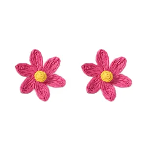 Dettaglio di orecchini a margherita in rafia rosa con petali intrecciati a mano e cuore
